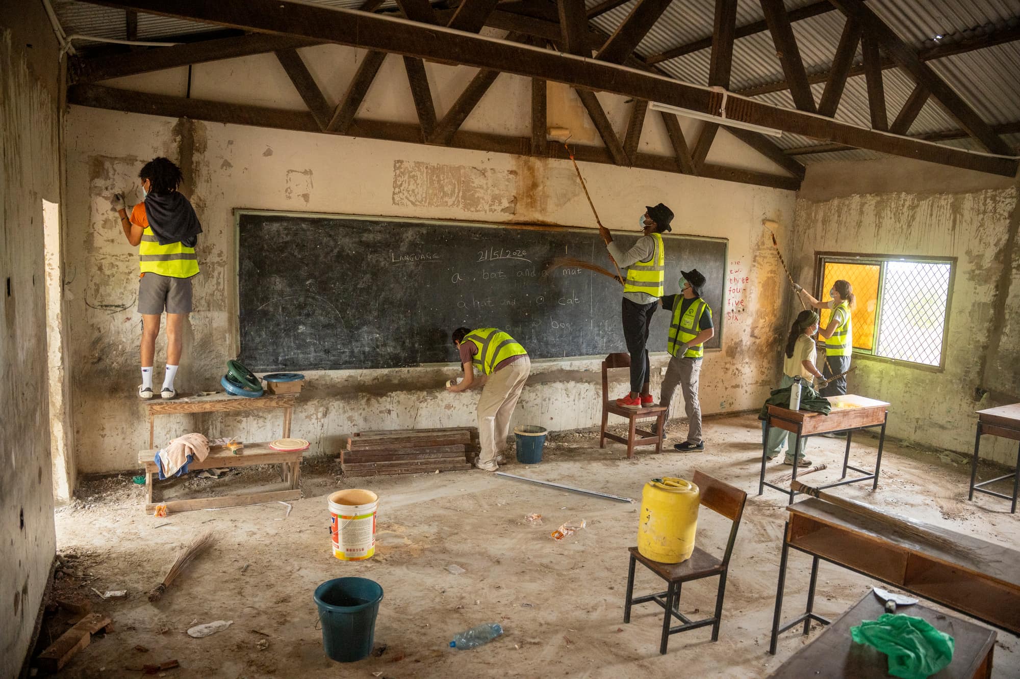 Trekkers in safety vests restoring a classroom, painting walls around the blackboard
