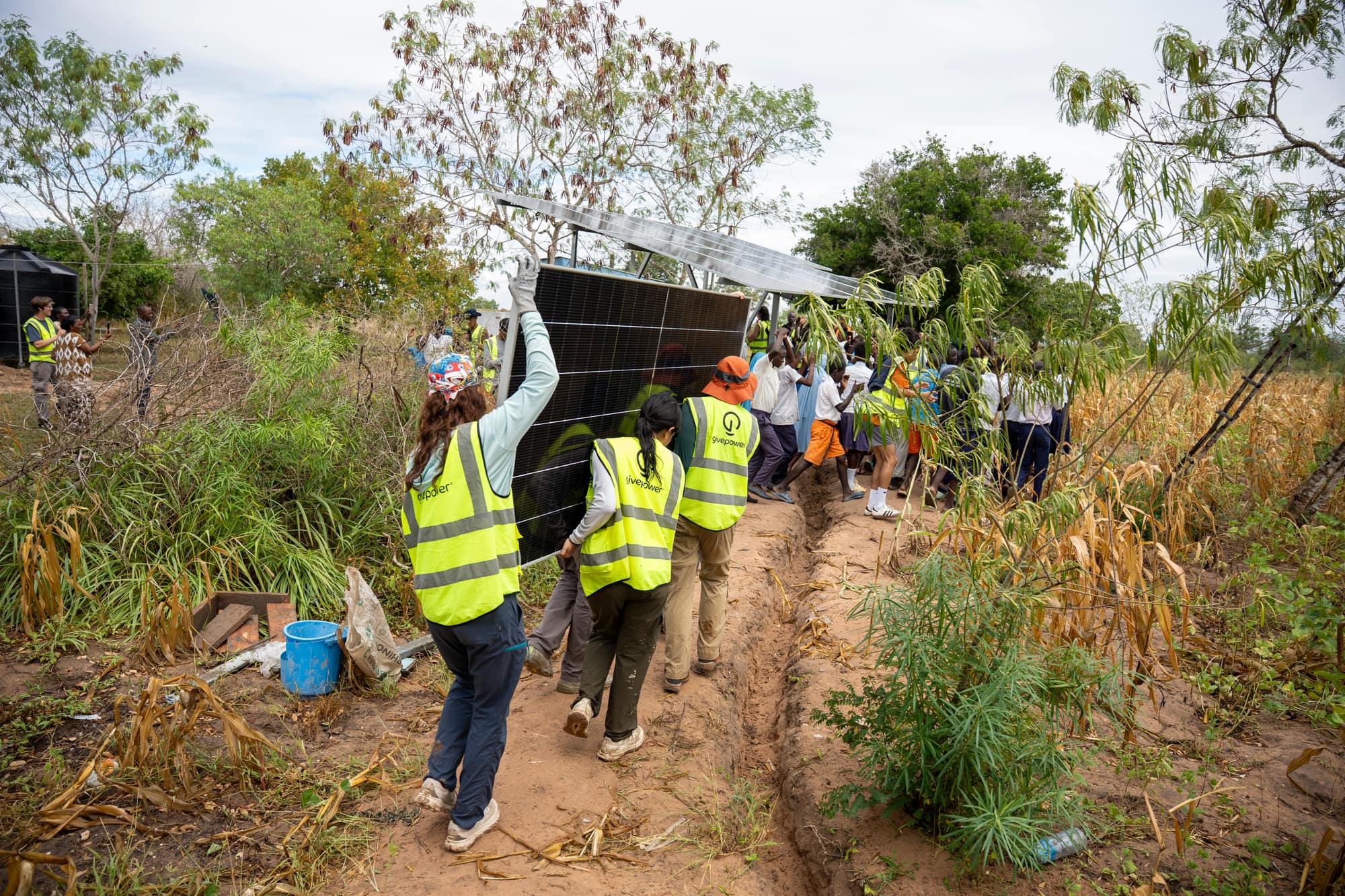 UT GivePower volunteers carrying a solar panel along a freshly dug trench to an install site in Kilifi County, Kenya