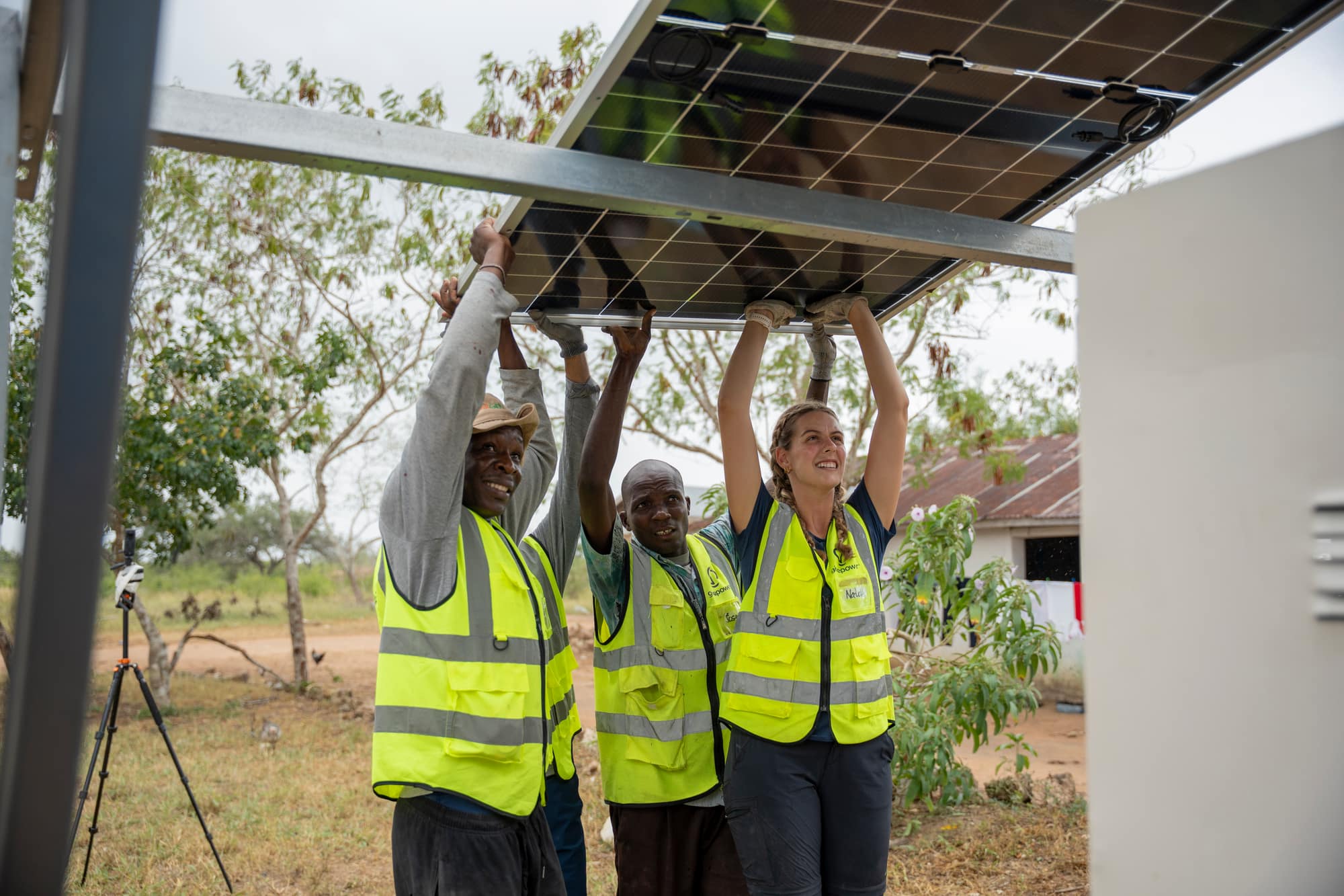 A UT GivePower trekker and local partners lifting a solar panel overhead into its rack during an install in Kenya