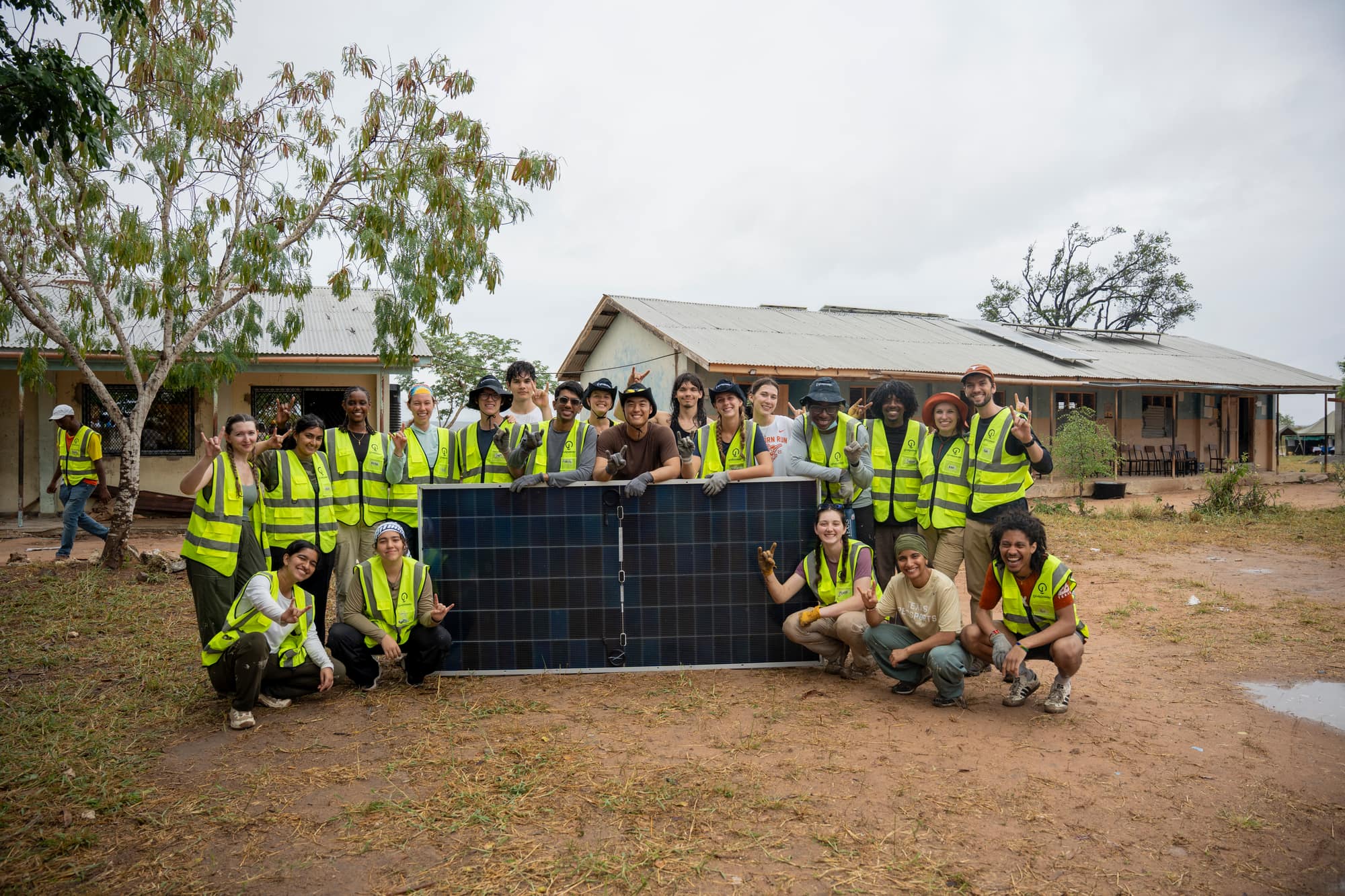 UT GivePower trekkers throwing horns up behind a solar panel after an install in Kenya